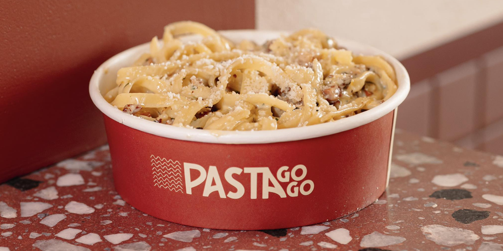 A bowl of freshly cooked creamy pasta topped with parmesan, served in a branded Pasta GoGo takeaway container. Captured on a red terrazzo counter inside the Hawthorn store, the dish features house-made pasta tossed with mushrooms, cracked pepper and a rich cream sauce — part of PastaGoGo’s made-to-order menu available in Melbourne.