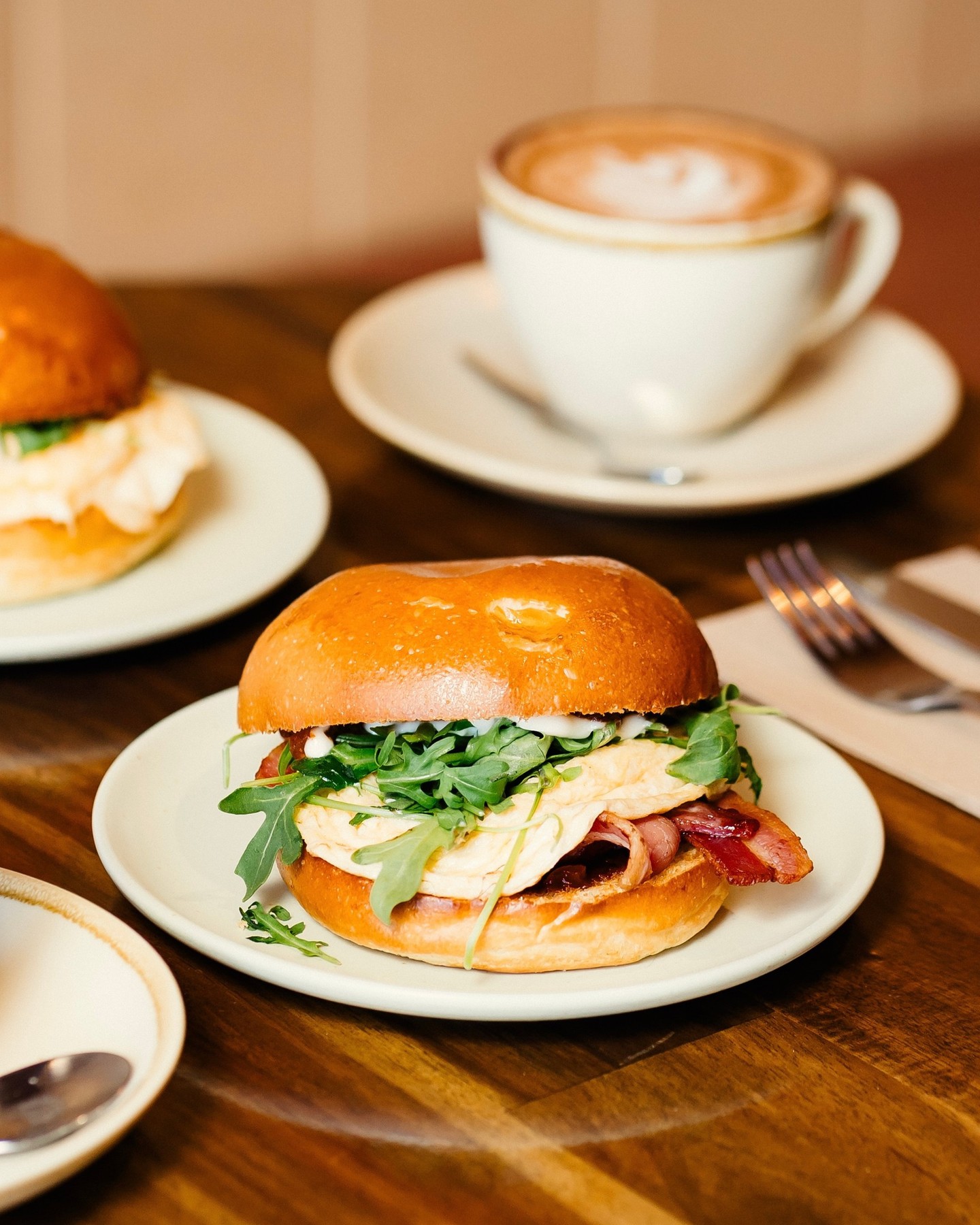 Freshly brewed St Ali coffee served alongside a brioche breakfast roll filled with soft scrambled eggs, crispy bacon and rocket, photographed at Miss Felix café in St Kilda. The warm, coastal setting and golden tones capture Melbourne’s signature brunch culture and beachside dining vibe.